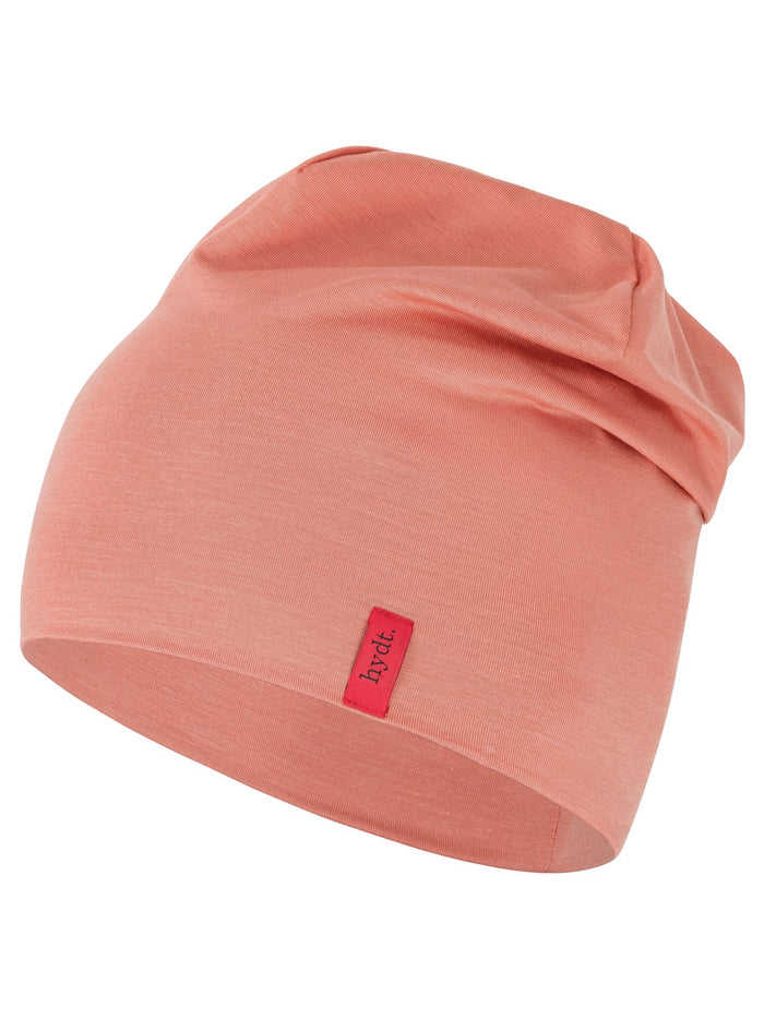 Korallenrote Chemo-Mütze (Beanie) der Marke hydt. aus weichem Jerseymaterial, leicht gerafft fallend mit rotem Marken-Label an der Seite.
