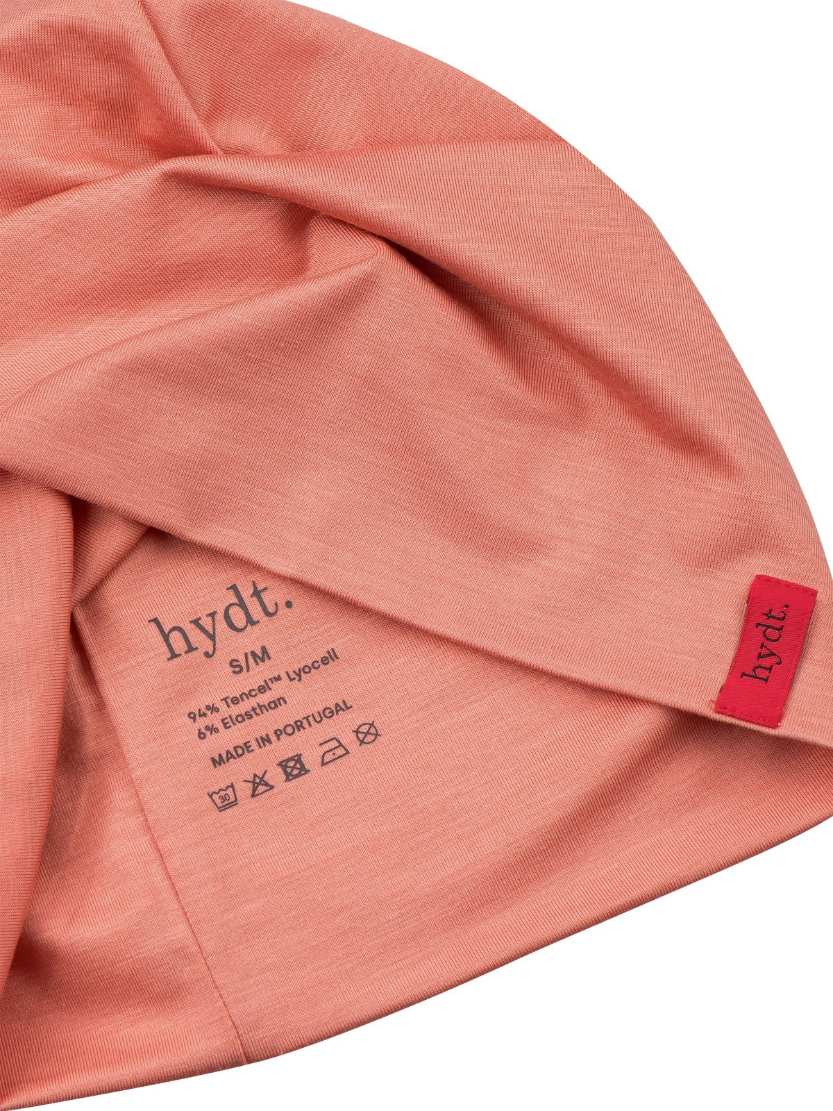 Detailaufnahme der Innenseite der korallenroten hydt. Mütze: Gedruckte Materiallabel, Made in Portugal und Pflegehinweisen.