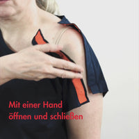 Das Video zeigt eine Frau die sich adaptives T-Shirt mit Schulteröffnung mit einer Hand zuknöpft